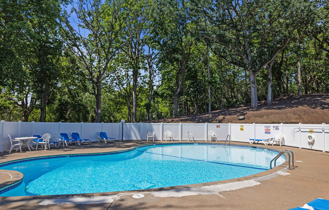 a swimming pool with chairs around it and trees in the background