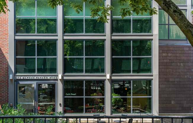 The exterior of a building with a glass facade and a tree in front.