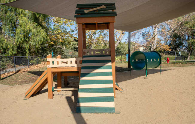 A playground with a wooden structure and a green slide.