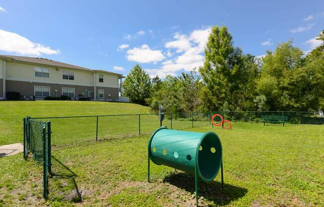 A green cylindrical object is in the foreground of a grassy area with a building in the background.