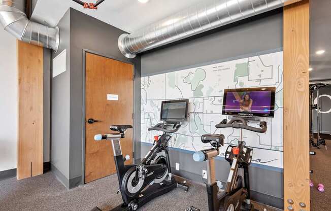 A room with a bike workout station and a TV screen showing a woman exercising.