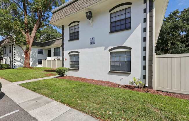 A white house with a brown roof and a small tree in front.