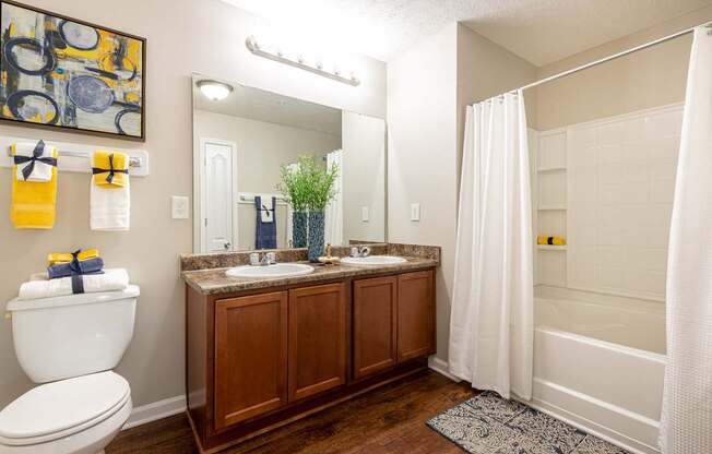 A bathroom with a white toilet, a sink with a brown cabinet, and a shower with a white curtain.