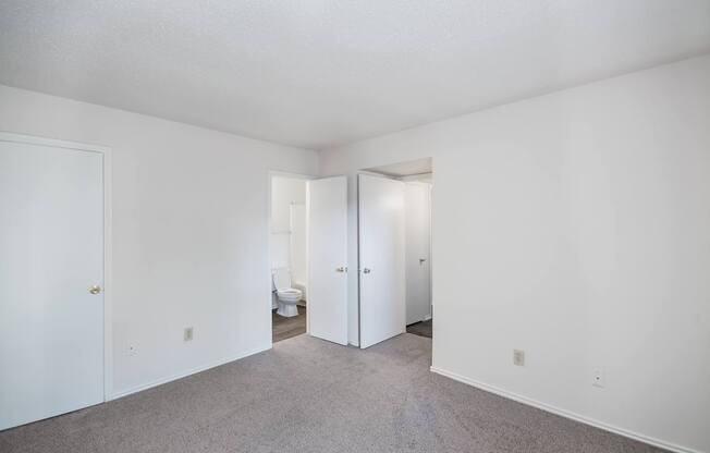 A white room with a carpeted floor and two open doors.
