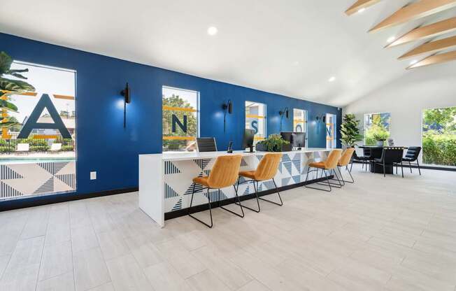 A room with a white desk and chairs with a blue wall and windows.