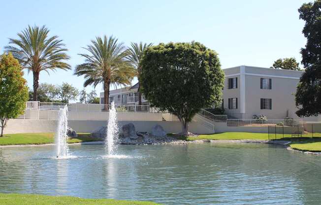 A fountain in the middle of a pond in front of a building.