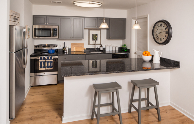 Kitchen with dark cabinets, quartz counters, and a peninsula with two chairs behind it.