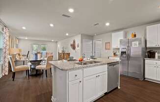 a white kitchen with a large island and a stainless steel refrigerator