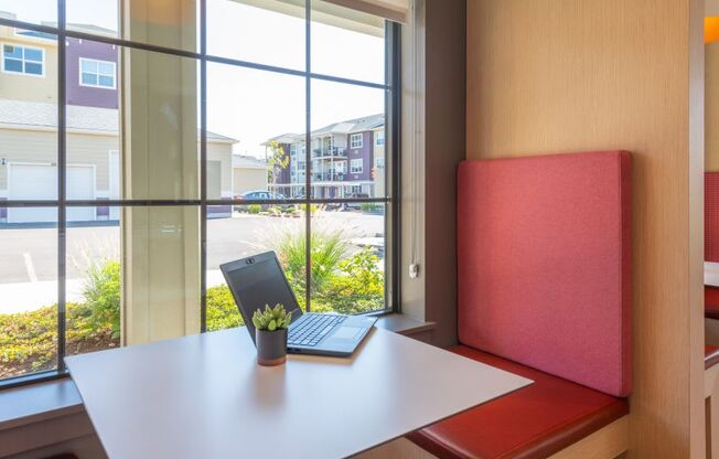 a desk with a laptop and a red chair in front of a window