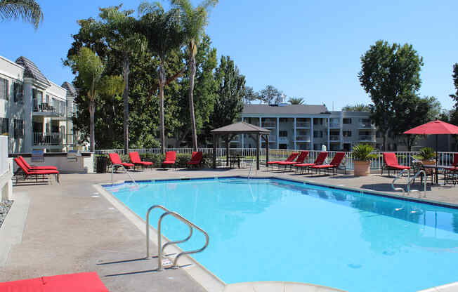 A swimming pool surrounded by red chairs and trees.