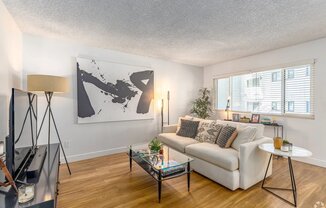 A living room with a white couch, a coffee table, and a large abstract painting on the wall.