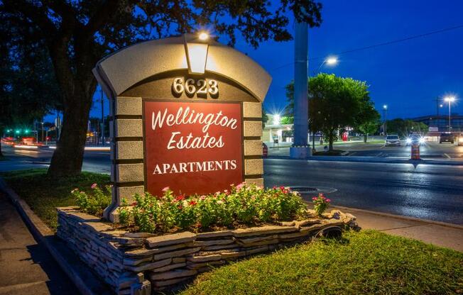 A sign for Wellington Estates Apartments is lit up at night.