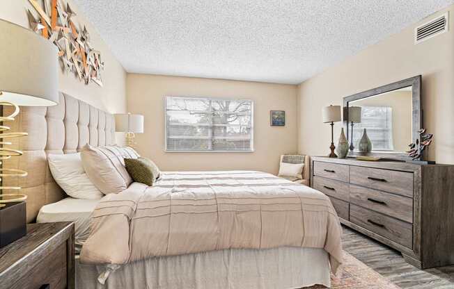 A bedroom with a large bed, a mirror, and a wooden dresser.