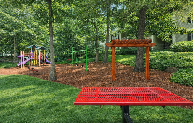 A red picnic table sits in the middle of a playground.