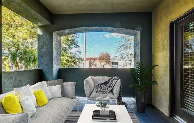 A living room with a grey couch, a white coffee table, and a large window with a view of trees.