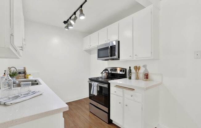 a white kitchen with white cabinets and a black microwave at Camino de Oro Apartments, Torrance, CA