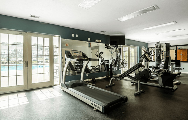 a gym with cardio equipment and a pool in the background