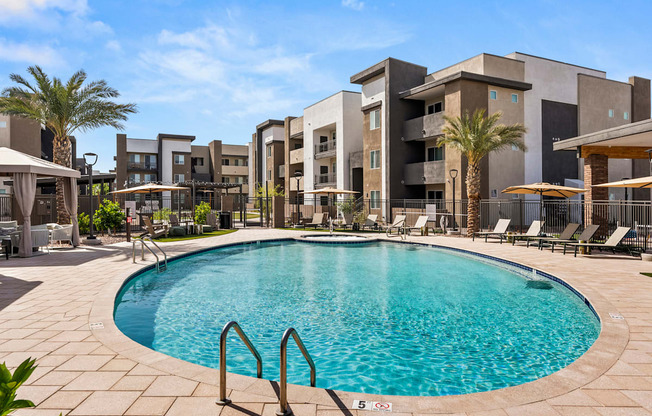 A swimming pool surrounded by lounge chairs and umbrellas in front of a modern building.