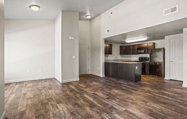 an empty living room with a kitchen with a refrigerator