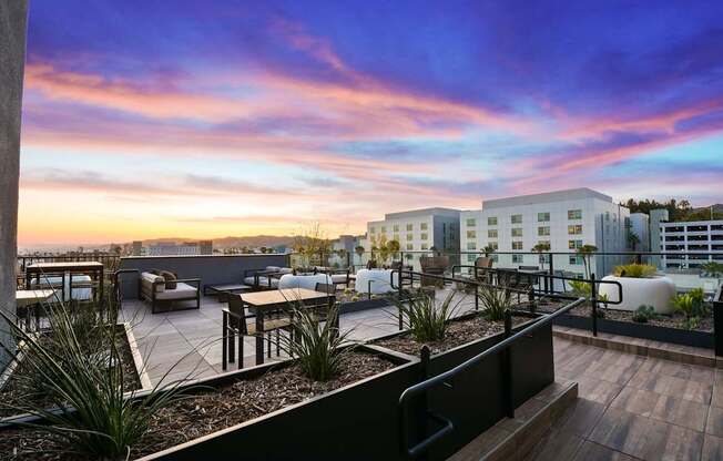 A rooftop patio with a table and chairs overlooking a cityscape at sunset.