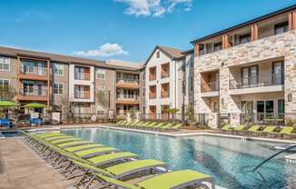 an outdoor swimming pool with yellow lounge chairs in front of an apartment building