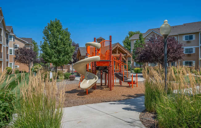 A playground with a slide and a play structure in the middle of a grassy area.