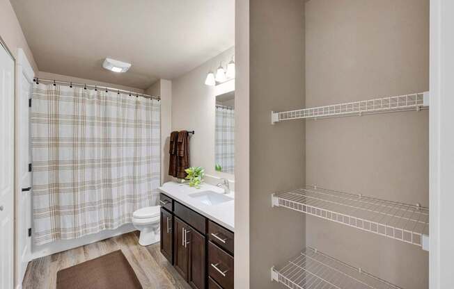 A bathroom with a shower curtain, toilet, sink, and shelves.