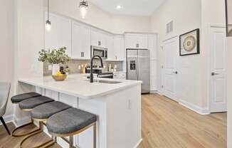 A kitchen with white cabinets and a white island with a vase of flowers on it.