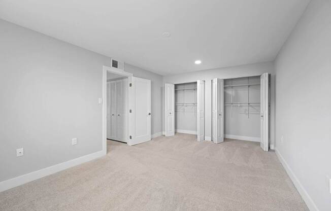 A room with white walls and carpeted floor with a white door on the left.