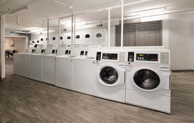 a row of white washers and dryers in a laundry room