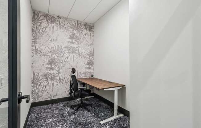 A small room with a desk and a plant pattern wallpaper.