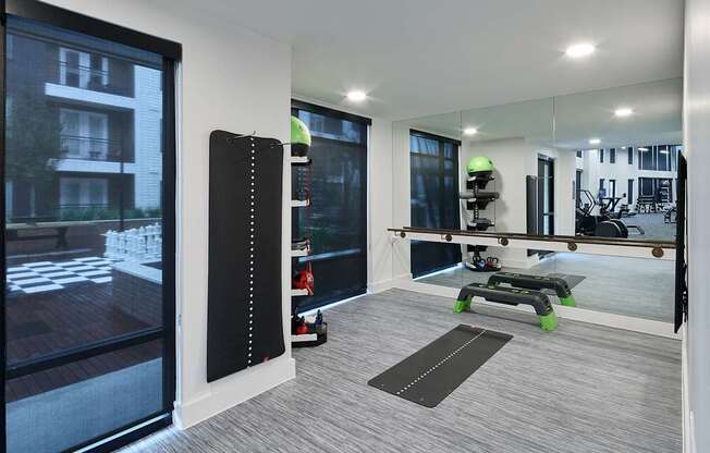 A modern room with a large mirror, a yoga mat, and a view of a building outside.