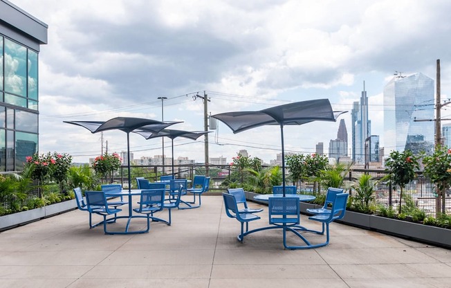 A patio with blue chairs and umbrellas overlooking a city skyline.