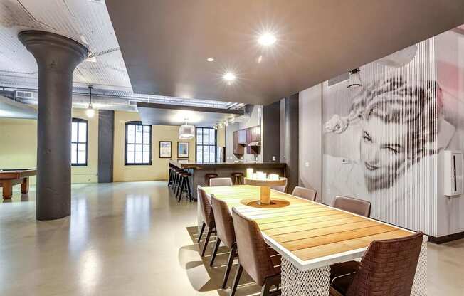 A long wooden table is surrounded by chairs in a room with a large poster on the wall.