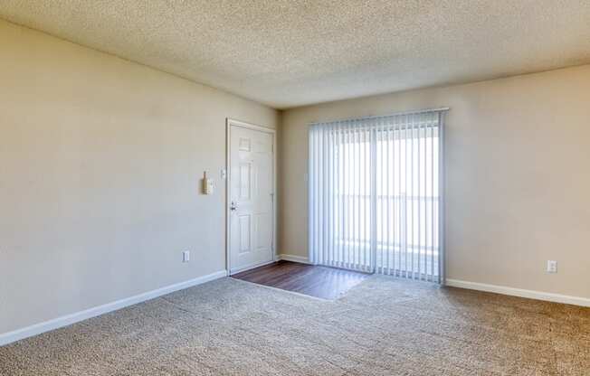 the spacious living room of an apartment with a large window and a door