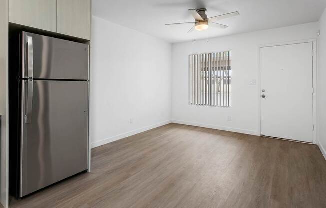 A room with a stainless steel refrigerator and wooden flooring.