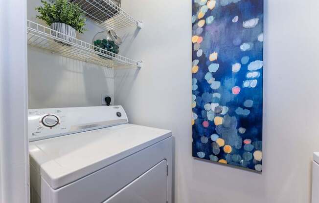A washing machine is sitting next to a wall with a painting of blue and orange circles.