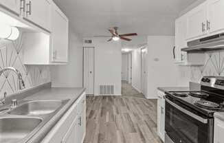 an empty kitchen with white cabinets and stainless steel appliances and a ceiling fan