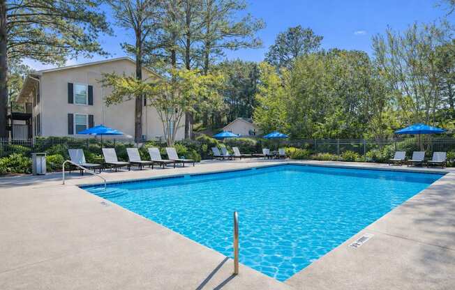 A swimming pool surrounded by trees and lounge chairs.