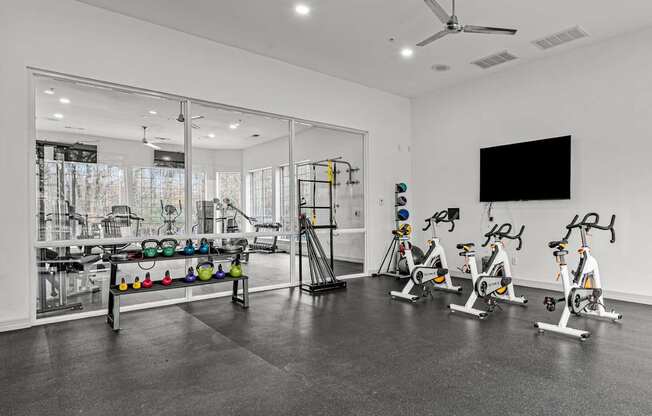 A room with a black floor and white walls has exercise bikes and a television.