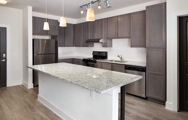 A kitchen with a granite countertop and dark brown cabinets.