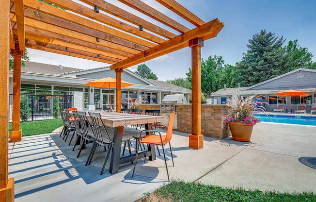 A wooden pergola with a table and chairs is in the foreground of a patio area.