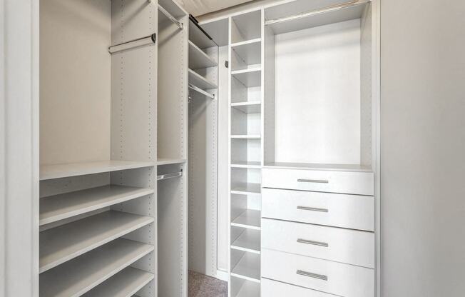 a walk in closet with white shelves and a window