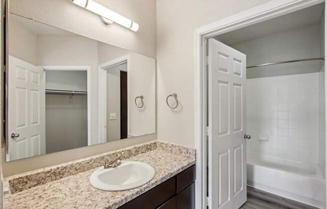 A bathroom with a sink, mirror, and bathtub.