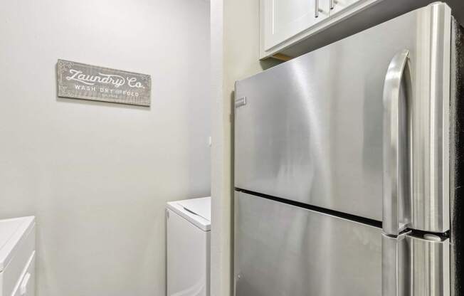 A stainless steel refrigerator and washing machine in a laundry room.