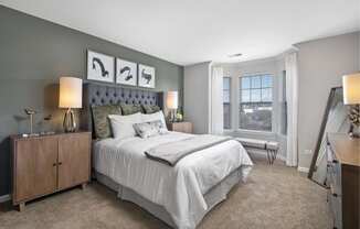 Furnished model bedroom with a queen sized bed and oversized bay windows
