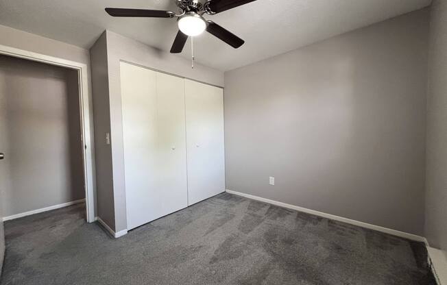 an empty living room with a ceiling fan and a closet