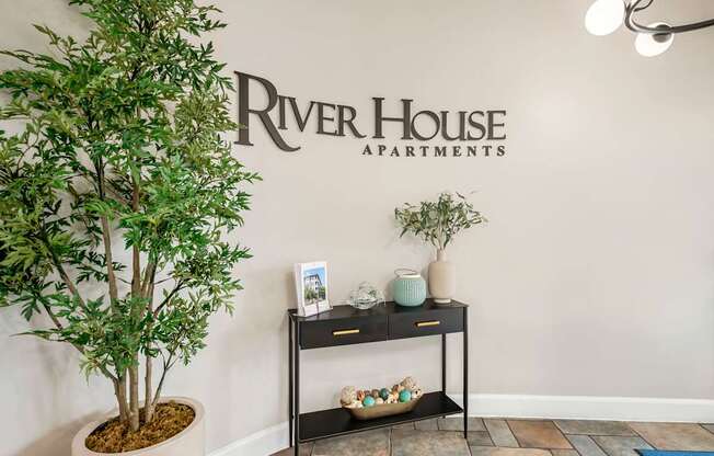 A River House Apartments lobby with a potted tree and a small table with decorative items.