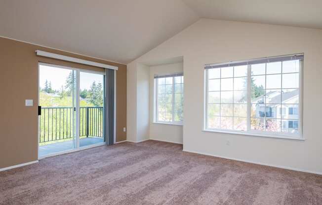 an empty living room with large windows and carpeting