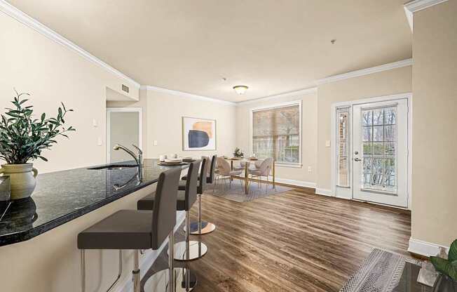 A kitchen with a black counter top and a dining area with a table and chairs.